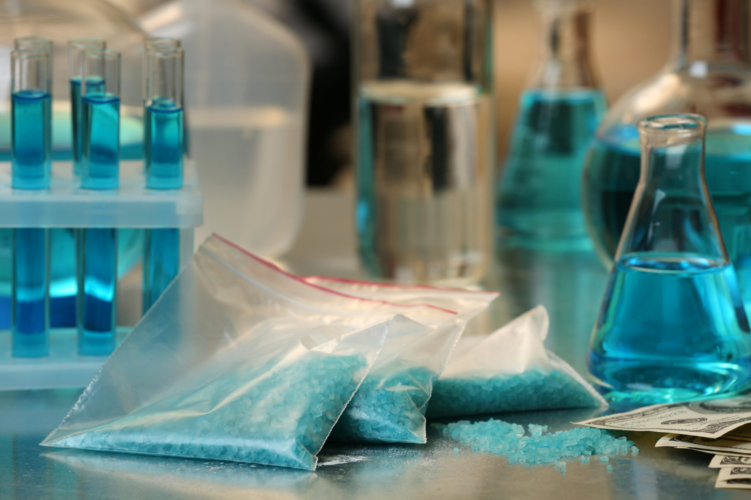 Drug laboratory: blue methamphetamine and money on table close up