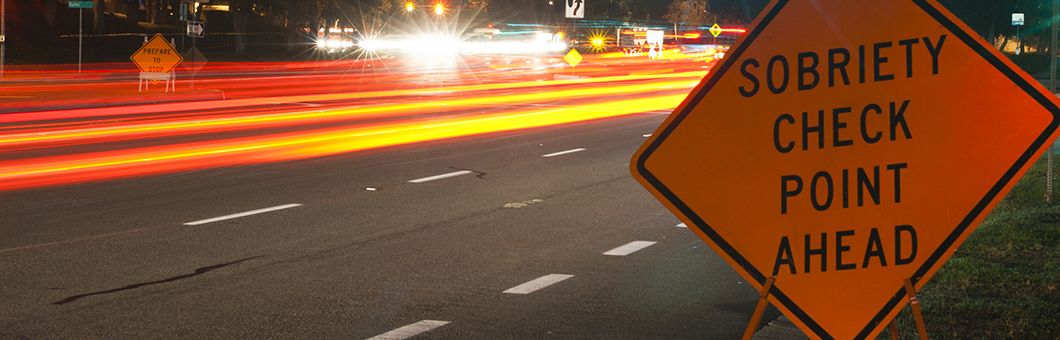 Sobriety checkpoint sign with vehicle light trails approaching on road